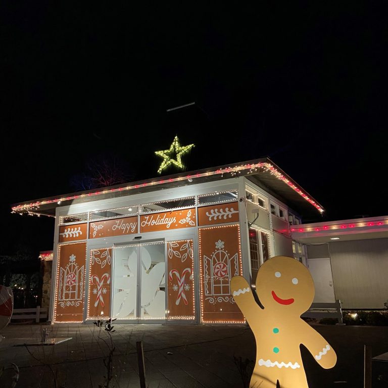 cutout gingerbread person waving in front of the teahouse decorated like a gingerbread house