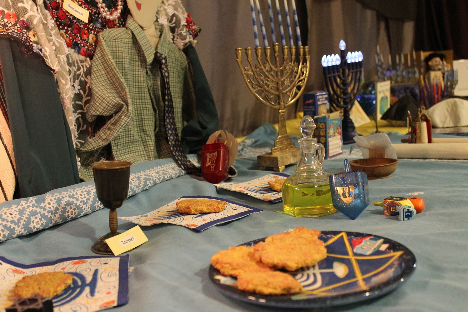 Museum display of Hanukkah table setup during celebratin with food and menorahs