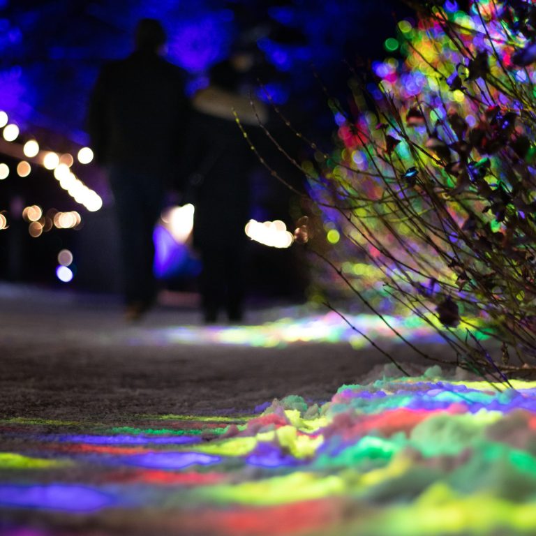 Low angle of rainbow lights across a path. Two people walk in the distance