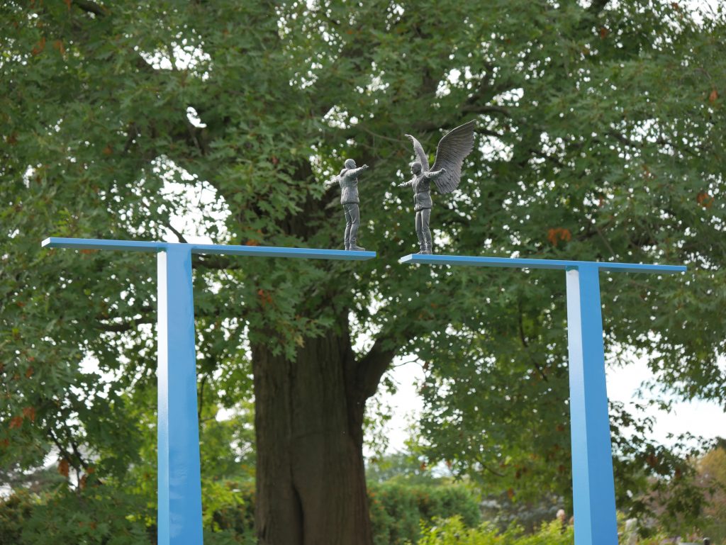 reverie sculpture, two blue T shaped beams. Two small fairy figures stand on the edge facing eachother