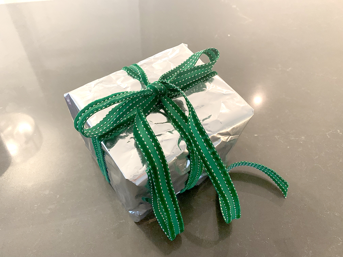 box wrapped with shiny metalic material and tied with a green ribbon