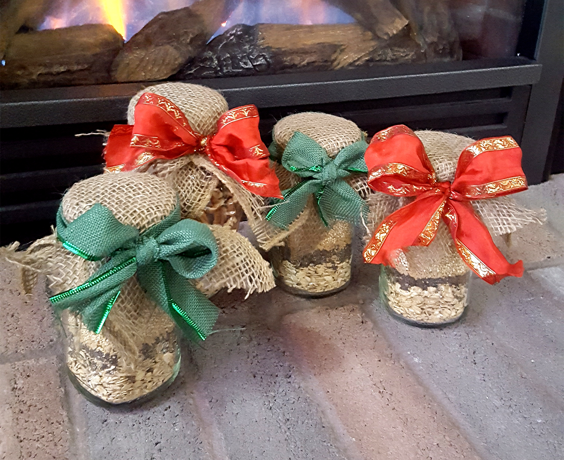 four handmade gifts in jars with food mix inside, decorated with burlap and ribbon