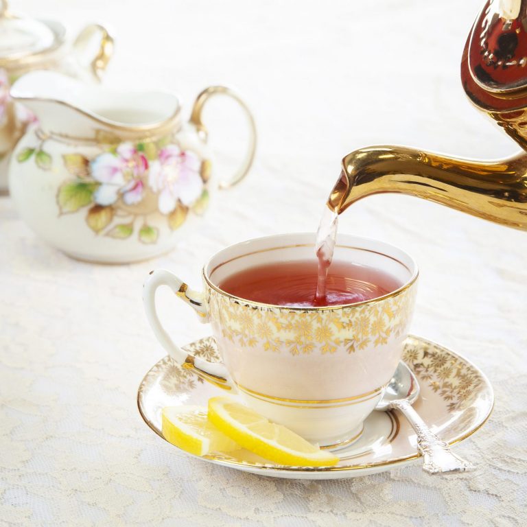 pouring tea into fine china cup with formal high tea setup